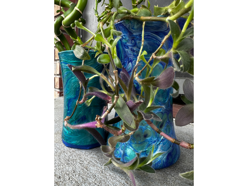 Two glass vases wrapped in teal and blue paint skins, holding plants